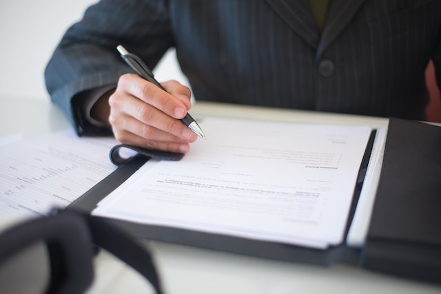 person in a suit holding a pen to sign a contract in front of them